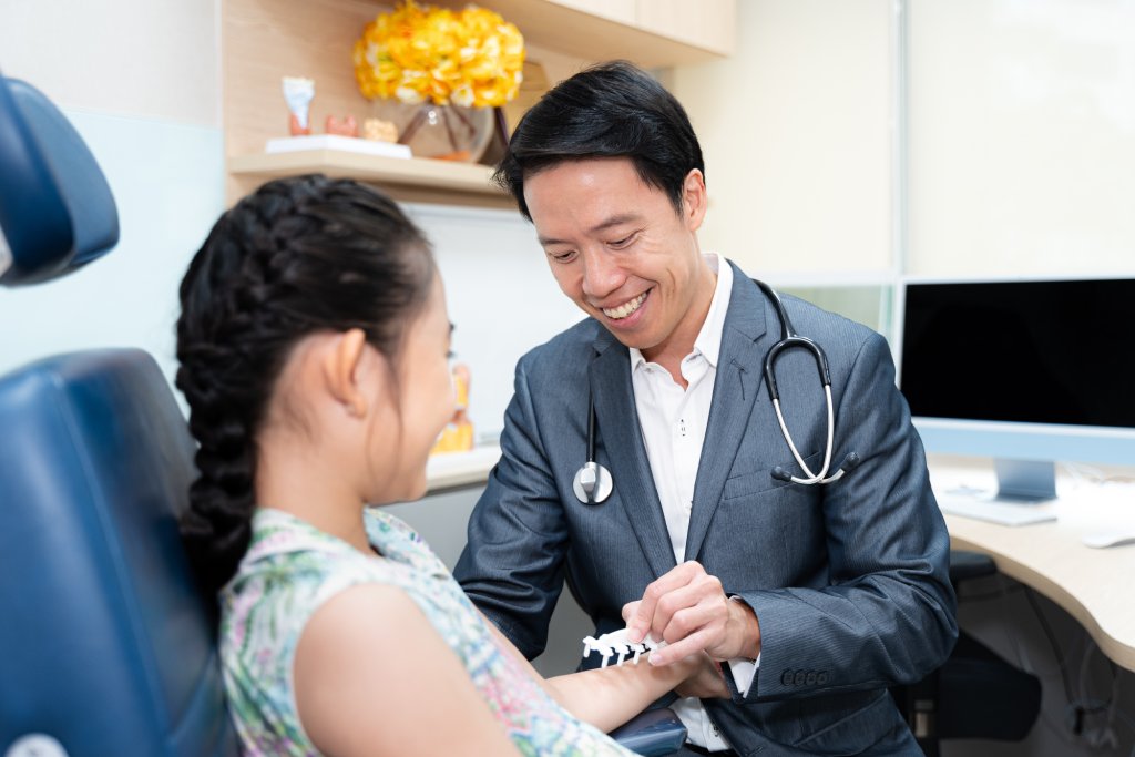 Dr. Chua in a suit examines a young patient set in a modern medical office with computers