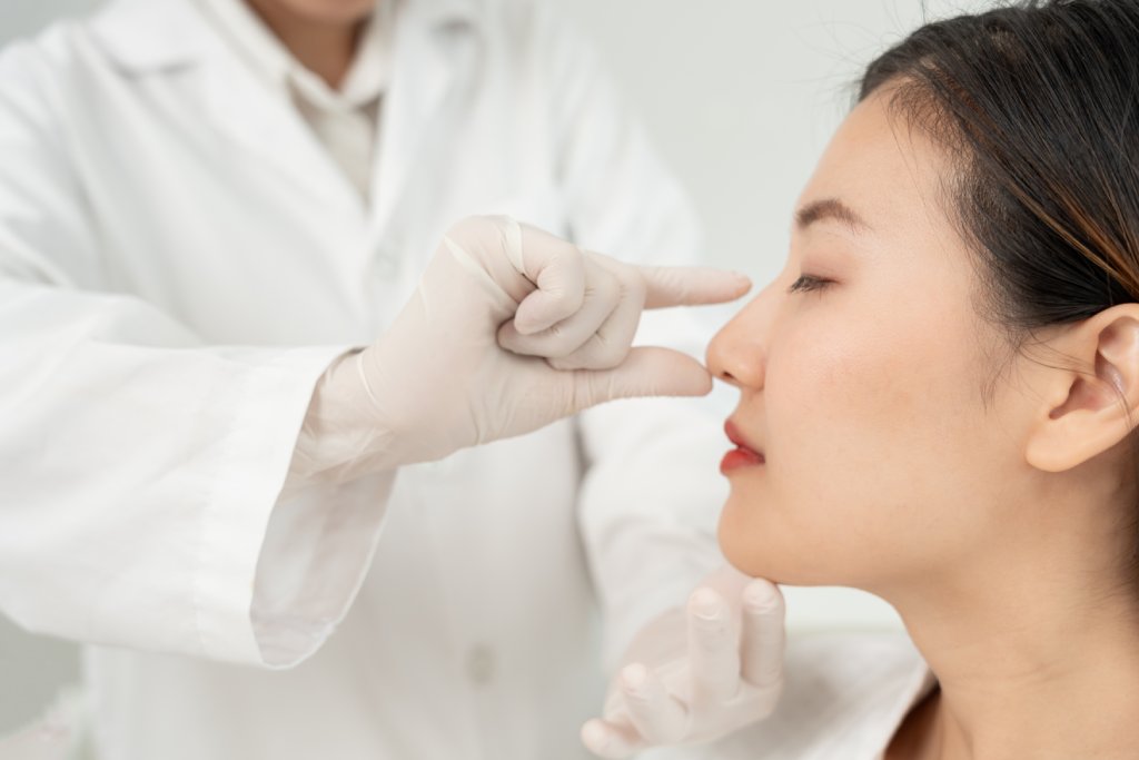 Healthcare professional wearing gloves and a white coat demonstrates a procedure near a patients ear