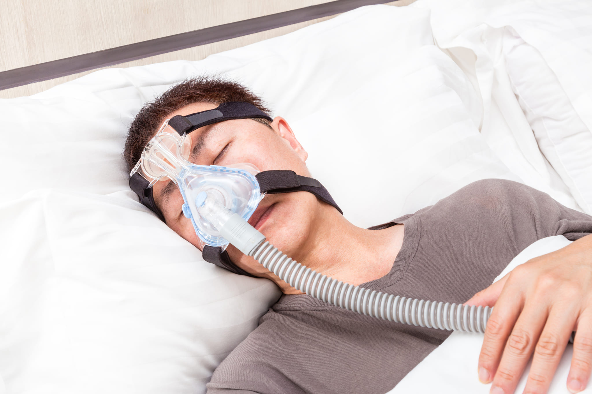 middle age asian man sleeping his bed wearing cpap headgear mask connected air hose